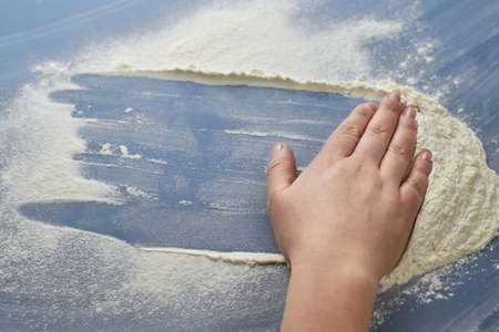 Woman's hand removes flour on blue background, the theme of cooking.の写真素材