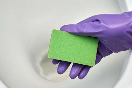Woman's hand in a glove washes the toilet bowl with a sponge, sanitizing and cleaning the toilet room.の写真素材