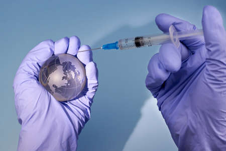 Woman's hands in medical gloves is holding a planet earth globe and a syringe, the concept of...