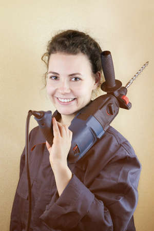Smiling beautiful woman in workwear with a puncher near the wall, toned photo.