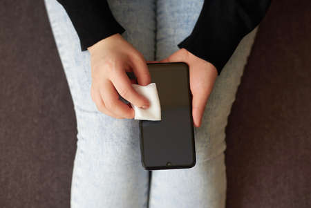 Woman wipes the screen of a mobile phone with an alcohol napkin at home, top view.の写真素材