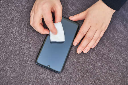 Woman wipes the screen of a mobile phone with an alcohol napkin at home, top view.