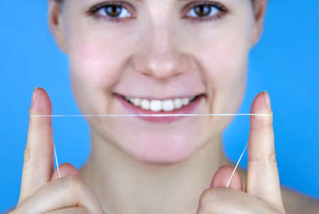 Smiling woman holding dental floss in front of her on a blue background.