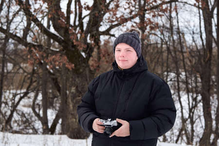 Man in a jacket and a hat with retro camera in winter forest.