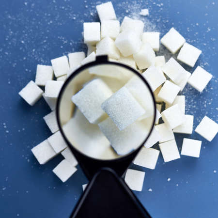 Checking sugar cubes with a magnifying glass on a blue background.の写真素材