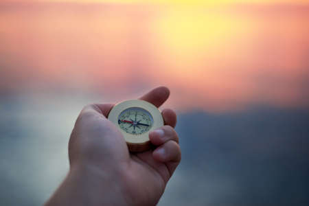 Man's hand with a compass on the sea coast at sunrise. Travel concept.の写真素材