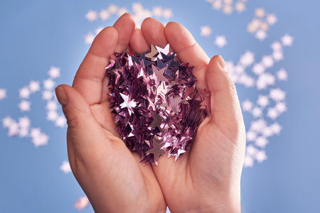 Pink glittering confetti in the hands of a woman on a blue background, Christmas and celebration concept.の写真素材