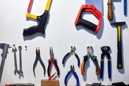 A set of different tools hanging on a white wall.