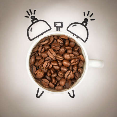 Cup of coffee filled with coffee beans in the shape of an alarm clock, the concept of morning wake up.の写真素材