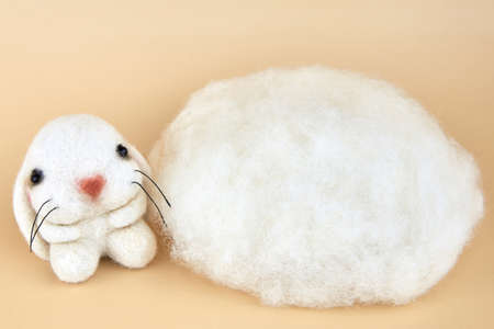 Handmade felted bunny near a piece of wool on a beige background.の写真素材