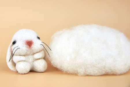 Handmade felted bunny near a piece of wool on a beige background.の写真素材