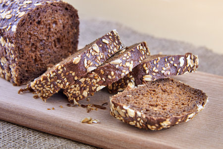 Dark rye sliced bread with whole sunflower seeds, flaxseeds and oatmeal on top on a board.の写真素材