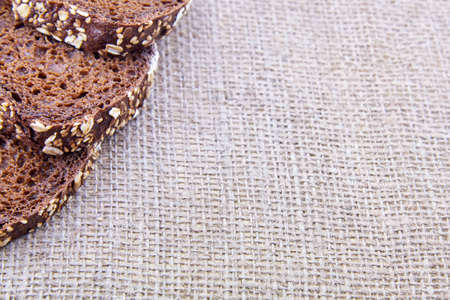 Slices of dark rye bread with whole sunflower seeds, flaxseeds and oatmeal on top on sackcloth, copy...