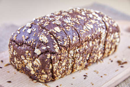 Dark rye bread with whole sunflower seeds, flaxseeds and oatmeal on top on a board.の写真素材