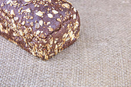 Whole dark rye bread with whole sunflower seeds, flaxseeds and oatmeal on top on sackcloth, copy space.の写真素材