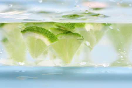 Pieces of lime float in a glass of water, close-up, backdrop.の写真素材