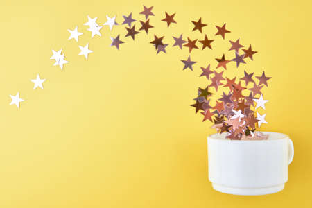 Confetti stars fly out of a cup on a yellow background.の写真素材