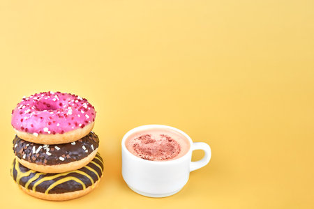 Three bright donuts near a cup of coffee on a yellow background, copy space.の写真素材