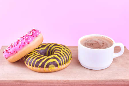 Three bright donuts with a cup of coffee on a wooden board on a pink background, copy space.