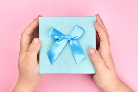 The boy's hands are holding a gift box with a bow on a pink background.の写真素材