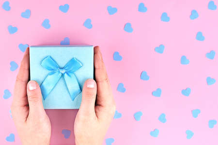 Paper gift box with a bow in the woman's hands on a pink background with confetti hearts.の写真素材