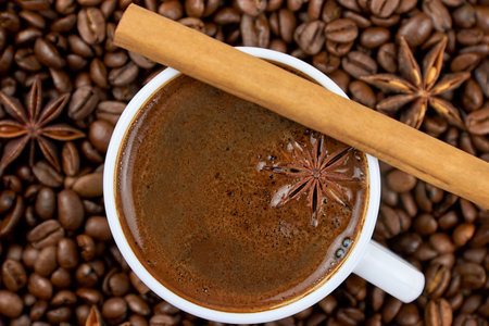 A cup of coffee with star anise and cinnamon on the background of coffee beans, close-up.の写真素材