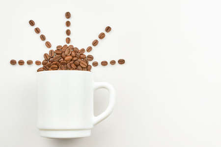 Cup and grains of coffee in the shape of the sun on a light background, copy space.の写真素材