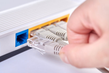 The hand inserts the Internet cable into the router, close-up.