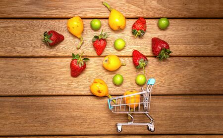 grocery carts and summer fruits on the wooden floor. plum loquat and strawberries