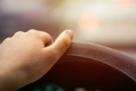 one hand holding car steering wheel on roadの写真素材