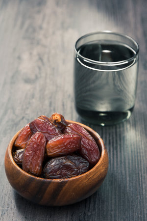 dried dates in a bowl and a glass of water behind it. In Islam, it is consumed to break the fast.の写真素材