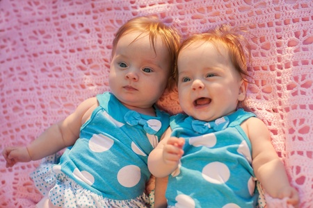 Sweet little  twins lying on a pink blanket  They in blue dress with white polka dots の写真素材