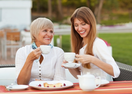 adult mother and daughter drinking tea or coffee and talking outdoorsの写真素材