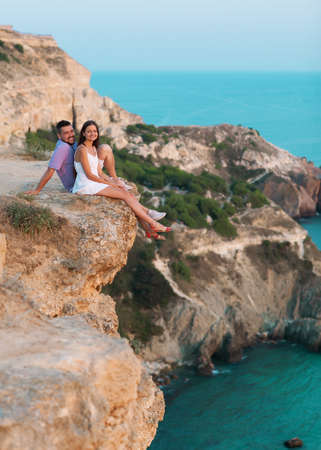 Couple sitting and laughing on the sand of the beach at sunset with the mountains の写真素材