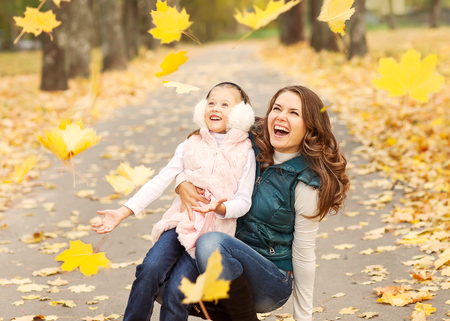 Mother and daughter having fun in the autumn park among the falling leaves.の写真素材