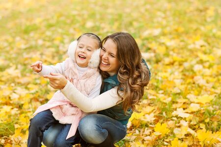 Mother and daughter having fun in the autumn park among the falling leaves.の写真素材