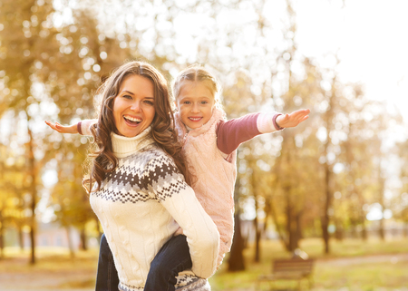 Mother giving daughter piggyback ride in autumn woodlandの写真素材
