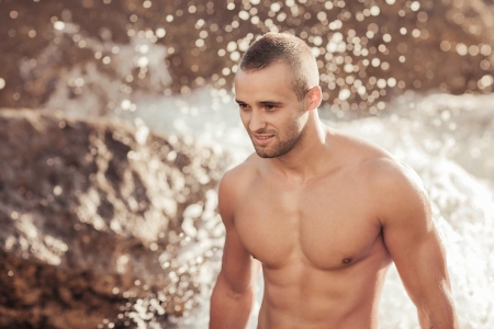 Portrait of a handsome young muscular man in swimtrunks with water ocean backgroundの写真素材