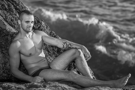 Portrait of a handsome young muscular man in swimtrunks with water ocean backgroundの写真素材