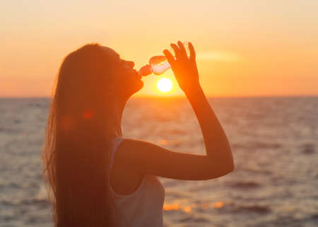 Woman drinking from a Water Bottle at Sunsetの写真素材