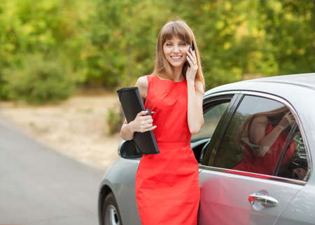 businesswoman talking on the phone while standing near his red carの写真素材