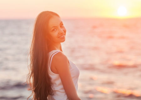 Enjoyment - free happy woman enjoying sunset. Beautiful woman in white dress embracing the golden sunshine glow of sunset with arms outspread and face raised in sky enjoying peace, serenity in natureの写真素材