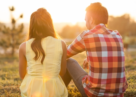 back view of young happy couple sitting on river at sunsetの写真素材
