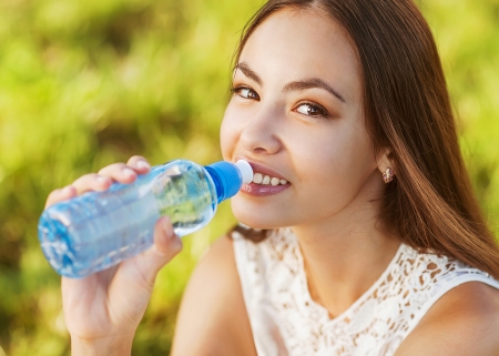Portrait of young beautiful dark-haired woman wearing blue t-shirt drinking water at summer green park.の写真素材