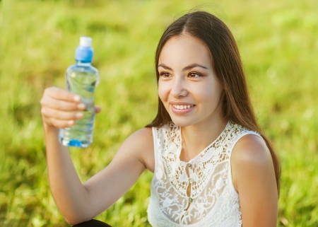 Portrait of young beautiful dark-haired woman wearing blue t-shirt drinking water at summer green park.の写真素材