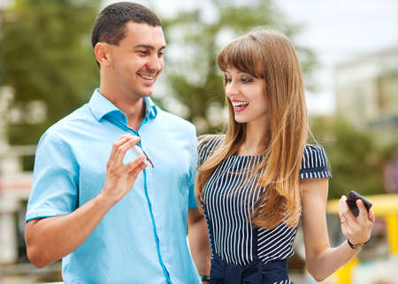 Young stylishly dressed couple on the street. He shows her something on his phone.の写真素材