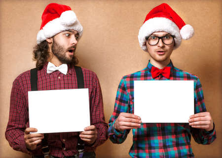 Christmas, x-mas, people, advertisement, sale concept - happy two man in santa helper hat with blank white board  Hipster style の写真素材