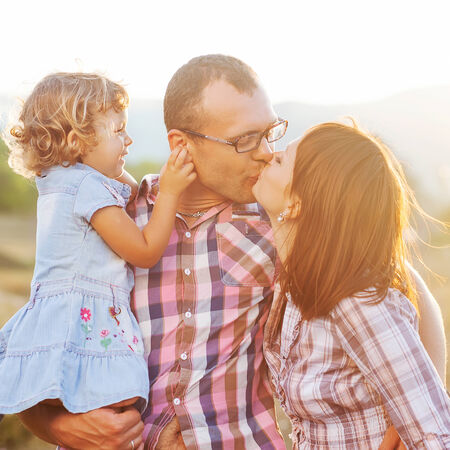 Happy mother, father and daughter in sunsetの写真素材