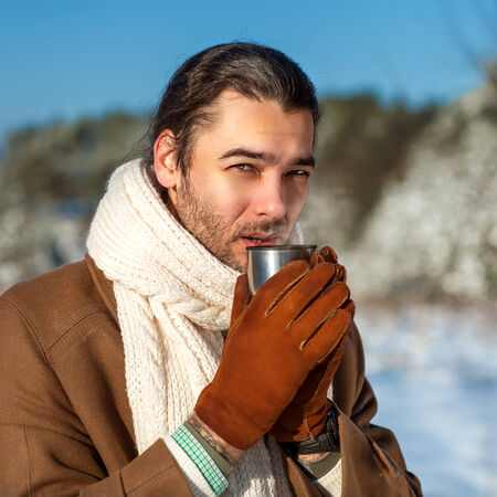 young attractive man drinking tea outside in winter time, close up portraitの写真素材