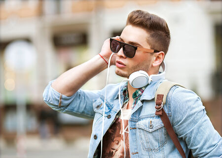 handsome fashion man listening to music on the grass in the parkの写真素材